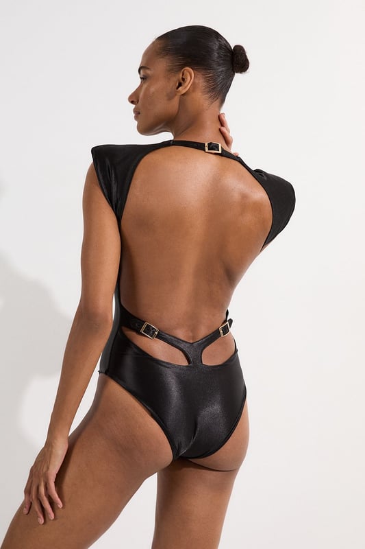 Make a statement poolside with this Wet Look Power Shoulder Cut Out Swimsuit. The architectural power shoulders create a bold, fashion-forward silhouette that commands attention, whilst the strategic cut-out detail adds intrigue to this one-piece design. Perfect for lounging by the pool at exclusive resorts or enjoying sunny beach days, this swimsuit transitions effortlessly from daytime swimming to sunset cocktails when paired with a flowing maxi skirt and statement jewellery. The sleek wet look fabric hugs your curves in all the right places, offering both style and comfort for your summer getaways.   Wet look finish catches the light. Bold power shoulder design Sleek cut-out detail Crew neckline offers coverage High-cut design elongates your figure