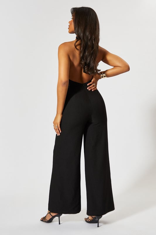 Chic halterneck design with elegant square neckline
        Straight leg silhouette for a flattering, contemporary look
        Backless feature adds a striking touch of glamour
        Wide-leg trousers create a flowing, sophisticated shape
        Linen-look fabric offers a textured finish with comfortable wear
    
    This MissPap jumpsuit combines effortless style with head-turning appeal. The halterneck design frames the dcolletage beautifully, whilst the backless detail creates a show-stopping moment when you turn around. Perfect for casual gatherings, style with strappy heels and statement earrings as seen on our model for evening drinks, or dress down with flat sandals and a woven tote for daytime events. The straight fit and wide-leg trousers create a relaxed yet polished silhouette that moves gracefully with every step. Layer with a cropped denim jacket for cooler evenings or add a waist belt to define your figure further. This versatile piece transitions seamlessly from family gatherings to sunset cocktails, making it an essential addition to your warm-weather wardrobe.