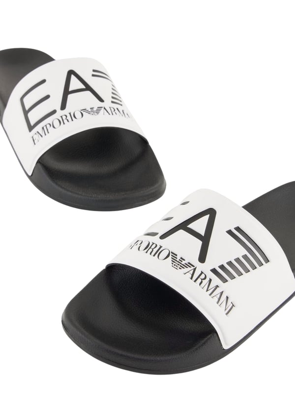 Die Slides von EA7 Emporio Armani vereinen stilvolles Design und hohen Tragekomfort. Sie zeichnen sich durch einen breiten Riemen mit einer eleganten Logo-Prägung sowie eine fein strukturierte Innensohle aus, die für zusätzlichen Komfort sorgt. Diese Slides sind die perfekte Wahl für entspannte Stunden am Pool oder Strand und lassen sich auch hervorragend ins Fitnessstudio mitnehmen. Der rutschfeste Gummiboden garantiert sicheren Halt und macht die Slides zu einem vielseitigen und praktischen Accessoire für sportliche und lässige Outfits.
