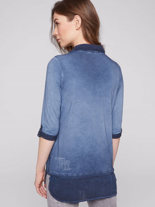 Legere blouse voor dames van het merk SOCCX. De blouse-details zorgen voor een geweldig lagenlook-effect. Bij de V-hals van het jersey-shirt is een blousekraag in ton-sur-ton materiaalmix ontworpen en onderaan een geknoopt blusenschoen. Het shirt heeft sportieve 3/4-mouwen met knoopstrips voor de opgerolde stijl, een decoratieve glitterprint aan de voorkant en een kleine druk aan de achterkant. Door de speciale kleurbehandeling krijgt het damesshirt een authentieke used-look.
