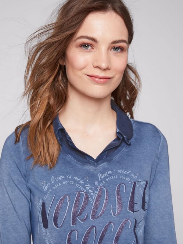 Legere blouse voor dames van het merk SOCCX. De blouse-details zorgen voor een geweldig lagenlook-effect. Bij de V-hals van het jersey-shirt is een blousekraag in ton-sur-ton materiaalmix ontworpen en onderaan een geknoopt blusenschoen. Het shirt heeft sportieve 3/4-mouwen met knoopstrips voor de opgerolde stijl, een decoratieve glitterprint aan de voorkant en een kleine druk aan de achterkant. Door de speciale kleurbehandeling krijgt het damesshirt een authentieke used-look.