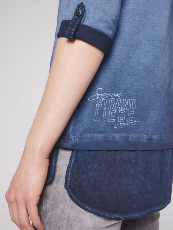 Legere blouse voor dames van het merk SOCCX. De blouse-details zorgen voor een geweldig lagenlook-effect. Bij de V-hals van het jersey-shirt is een blousekraag in ton-sur-ton materiaalmix ontworpen en onderaan een geknoopt blusenschoen. Het shirt heeft sportieve 3/4-mouwen met knoopstrips voor de opgerolde stijl, een decoratieve glitterprint aan de voorkant en een kleine druk aan de achterkant. Door de speciale kleurbehandeling krijgt het damesshirt een authentieke used-look.