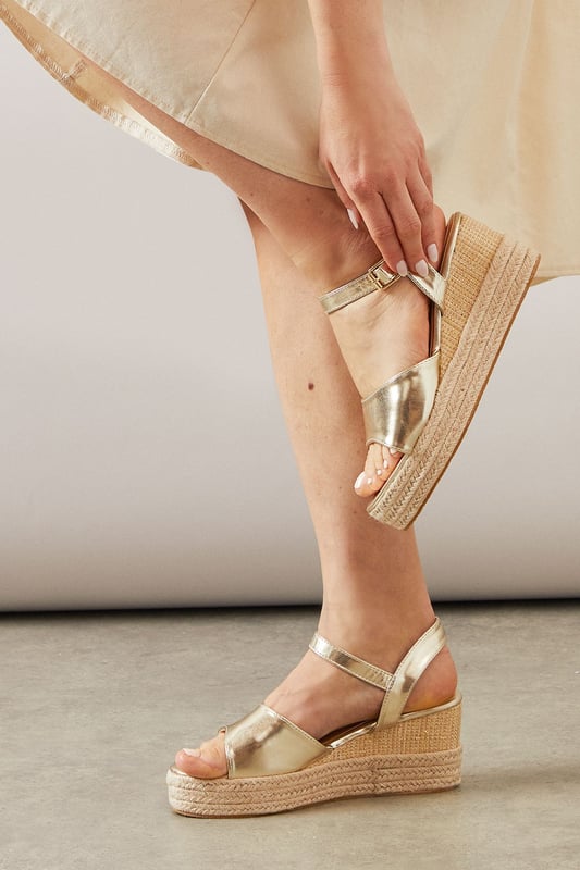 Striking high wedge design with approximately 8cm heel height for a glamorous lift
        Adjustable ankle strap with buckle fastening for a secure, customised fit
        Faux leather finish that offers both style and practicality
        Espadrille-style woven platform detail adding textural interest
        Open toe silhouette perfect for showcasing summer pedicures
    
    The Roxy High Wedge Sandals from Wallis combine sophistication with everyday comfort. The substantial wedge heel provides height without sacrificing stability, making these sandals ideal for long summer days that transition into evening gatherings. The clean lines and adjustable ankle strap create a flattering silhouette that pairs beautifully with flowing midi dresses, as shown, or with cropped trousers for a polished daytime look. These versatile sandals shine at casual garden parties, family lunches, or weekend shopping trips. The textured platform base adds a touch of Mediterranean flair, whilst the open toe design keeps them feeling fresh and seasonal. Perfect for the woman who desires a touch of glamour in her everyday wardrobe without compromising on comfort.