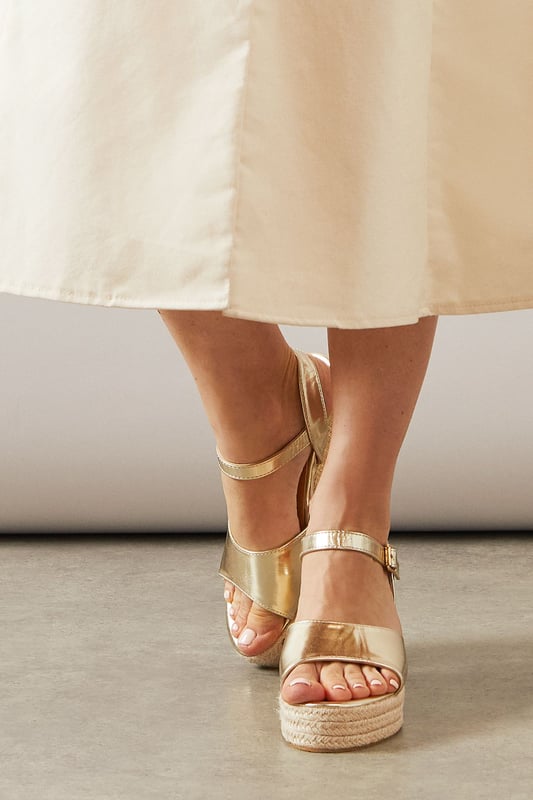 Striking high wedge design with approximately 8cm heel height for a glamorous lift
        Adjustable ankle strap with buckle fastening for a secure, customised fit
        Faux leather finish that offers both style and practicality
        Espadrille-style woven platform detail adding textural interest
        Open toe silhouette perfect for showcasing summer pedicures
    
    The Roxy High Wedge Sandals from Wallis combine sophistication with everyday comfort. The substantial wedge heel provides height without sacrificing stability, making these sandals ideal for long summer days that transition into evening gatherings. The clean lines and adjustable ankle strap create a flattering silhouette that pairs beautifully with flowing midi dresses, as shown, or with cropped trousers for a polished daytime look. These versatile sandals shine at casual garden parties, family lunches, or weekend shopping trips. The textured platform base adds a touch of Mediterranean flair, whilst the open toe design keeps them feeling fresh and seasonal. Perfect for the woman who desires a touch of glamour in her everyday wardrobe without compromising on comfort.
