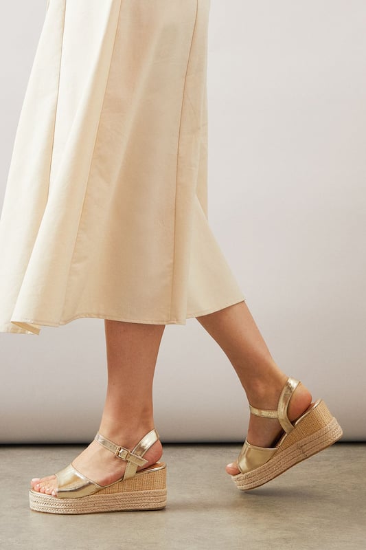 Striking high wedge design with approximately 8cm heel height for a glamorous lift
        Adjustable ankle strap with buckle fastening for a secure, customised fit
        Faux leather finish that offers both style and practicality
        Espadrille-style woven platform detail adding textural interest
        Open toe silhouette perfect for showcasing summer pedicures
    
    The Roxy High Wedge Sandals from Wallis combine sophistication with everyday comfort. The substantial wedge heel provides height without sacrificing stability, making these sandals ideal for long summer days that transition into evening gatherings. The clean lines and adjustable ankle strap create a flattering silhouette that pairs beautifully with flowing midi dresses, as shown, or with cropped trousers for a polished daytime look. These versatile sandals shine at casual garden parties, family lunches, or weekend shopping trips. The textured platform base adds a touch of Mediterranean flair, whilst the open toe design keeps them feeling fresh and seasonal. Perfect for the woman who desires a touch of glamour in her everyday wardrobe without compromising on comfort.