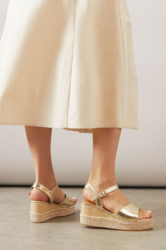 Striking high wedge design with approximately 8cm heel height for a glamorous lift
        Adjustable ankle strap with buckle fastening for a secure, customised fit
        Faux leather finish that offers both style and practicality
        Espadrille-style woven platform detail adding textural interest
        Open toe silhouette perfect for showcasing summer pedicures
    
    The Roxy High Wedge Sandals from Wallis combine sophistication with everyday comfort. The substantial wedge heel provides height without sacrificing stability, making these sandals ideal for long summer days that transition into evening gatherings. The clean lines and adjustable ankle strap create a flattering silhouette that pairs beautifully with flowing midi dresses, as shown, or with cropped trousers for a polished daytime look. These versatile sandals shine at casual garden parties, family lunches, or weekend shopping trips. The textured platform base adds a touch of Mediterranean flair, whilst the open toe design keeps them feeling fresh and seasonal. Perfect for the woman who desires a touch of glamour in her everyday wardrobe without compromising on comfort.