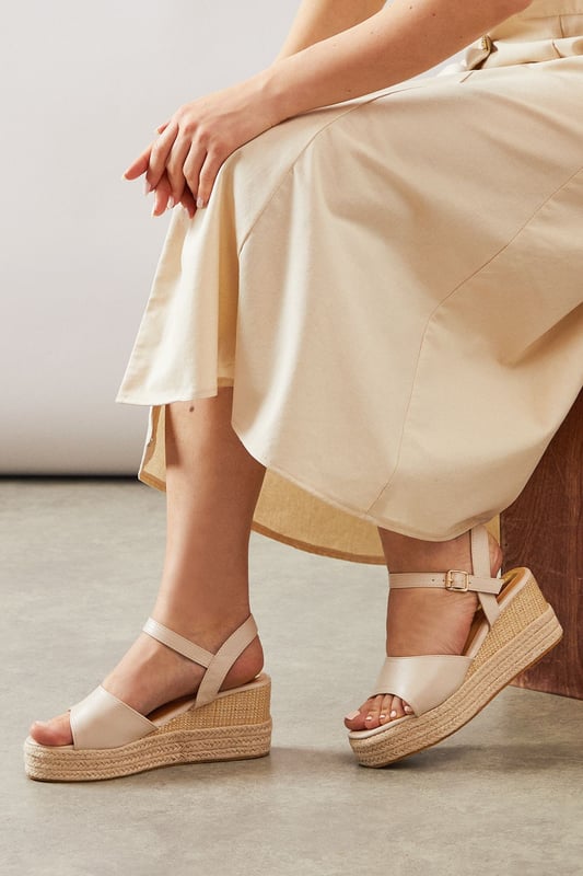 Striking high wedge design with approximately 8cm heel height for a glamorous lift
        Adjustable ankle strap with buckle fastening for a secure, customised fit
        Faux leather finish that offers both style and practicality
        Espadrille-style woven platform detail adding textural interest
        Open toe silhouette perfect for showcasing summer pedicures
    
    The Roxy High Wedge Sandals from Wallis combine sophistication with everyday comfort. The substantial wedge heel provides height without sacrificing stability, making these sandals ideal for long summer days that transition into evening gatherings. The clean lines and adjustable ankle strap create a flattering silhouette that pairs beautifully with flowing midi dresses, as shown, or with cropped trousers for a polished daytime look. These versatile sandals shine at casual garden parties, family lunches, or weekend shopping trips. The textured platform base adds a touch of Mediterranean flair, whilst the open toe design keeps them feeling fresh and seasonal. Perfect for the woman who desires a touch of glamour in her everyday wardrobe without compromising on comfort.