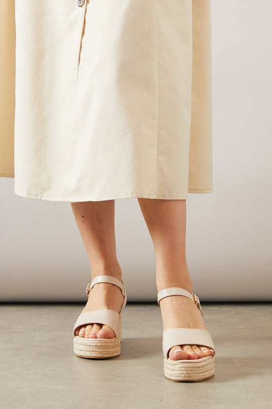 Striking high wedge design with approximately 8cm heel height for a glamorous lift
        Adjustable ankle strap with buckle fastening for a secure, customised fit
        Faux leather finish that offers both style and practicality
        Espadrille-style woven platform detail adding textural interest
        Open toe silhouette perfect for showcasing summer pedicures
    
    The Roxy High Wedge Sandals from Wallis combine sophistication with everyday comfort. The substantial wedge heel provides height without sacrificing stability, making these sandals ideal for long summer days that transition into evening gatherings. The clean lines and adjustable ankle strap create a flattering silhouette that pairs beautifully with flowing midi dresses, as shown, or with cropped trousers for a polished daytime look. These versatile sandals shine at casual garden parties, family lunches, or weekend shopping trips. The textured platform base adds a touch of Mediterranean flair, whilst the open toe design keeps them feeling fresh and seasonal. Perfect for the woman who desires a touch of glamour in her everyday wardrobe without compromising on comfort.