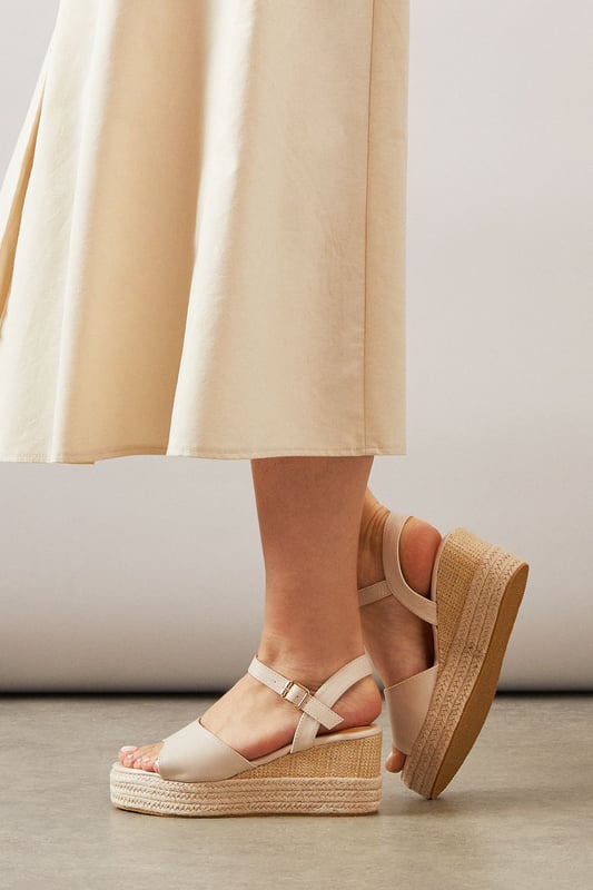 Striking high wedge design with approximately 8cm heel height for a glamorous lift
        Adjustable ankle strap with buckle fastening for a secure, customised fit
        Faux leather finish that offers both style and practicality
        Espadrille-style woven platform detail adding textural interest
        Open toe silhouette perfect for showcasing summer pedicures
    
    The Roxy High Wedge Sandals from Wallis combine sophistication with everyday comfort. The substantial wedge heel provides height without sacrificing stability, making these sandals ideal for long summer days that transition into evening gatherings. The clean lines and adjustable ankle strap create a flattering silhouette that pairs beautifully with flowing midi dresses, as shown, or with cropped trousers for a polished daytime look. These versatile sandals shine at casual garden parties, family lunches, or weekend shopping trips. The textured platform base adds a touch of Mediterranean flair, whilst the open toe design keeps them feeling fresh and seasonal. Perfect for the woman who desires a touch of glamour in her everyday wardrobe without compromising on comfort.