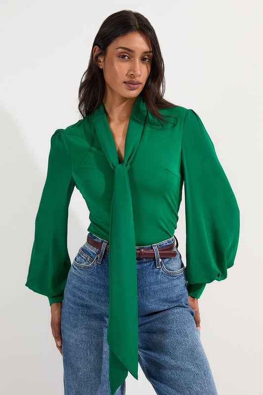 This Karen Millen bodysuit combines classic elegance with contemporary styling. The contrasting textures of jersey and georgette create visual interest, while the statement pussy bow adds a touch of feminine charm. The balloon sleeves provide dramatic volume balanced by the fitted bodice, creating a flattering silhouette. Perfect for family gatherings or casual work events, this bodysuit can be dressed down with tailored denim and flats for weekend brunches, or paired with a pencil skirt for more refined occasions. The secure bodysuit design eliminates the need for constant re-tucking, ensuring you maintain a sleek appearance throughout the day. A versatile wardrobe staple that offers both comfort and sophistication.  Jersey bodysuit featuring a georgette pussy bow detail Voluminous balloon sleeves with fitted cuffs and button detailing Round neckline Smooth, form-fitting designe