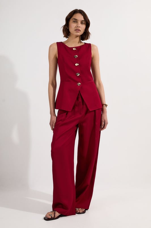 Ease into the new season, surrendering to the return of sunlit afternoons and a relaxed, carefree spirit. Discover contemporary cuts that can be mixed and matched effortlessly - creating a clean and sophisticated aesthetic.  This waistcoat reimagines traditional tailoring with its contemporary silhouette and striking button detail. The linen-viscose blend creates a structured yet breathable piece that maintains its shape beautifully throughout the day. Style with wide-leg trousers as shown for a relaxed daytime ensemble that balances structure with fluidity. For casual gatherings, layer over a crisp white shirt with sleeves rolled up and pair with your favourite straight-leg jeans and leather trainers. This versatile piece transitions effortlessly from office to weekend brunch, simply swap your footwear from flats to ankle boots as the occasion demands. The unique button placement and asymmetrical hem create a distinctive focal point that will refresh your everyday wardrobe staples.  Sleek tailored waistcoat featuring distinctive statement buttons for a contemporary twist Slim fit design with a flattering silhouette that accentuates the waistline Round neckline offering a sophisticated alternative to traditional V-neck waistcoats Asymmetrical hem with a modern front split detail for added visual interest Versatile sleeveless design perfect for layering throughout multiple seasons
