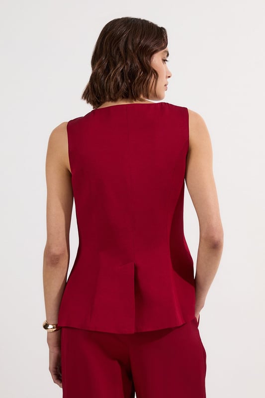 Ease into the new season, surrendering to the return of sunlit afternoons and a relaxed, carefree spirit. Discover contemporary cuts that can be mixed and matched effortlessly - creating a clean and sophisticated aesthetic.  This waistcoat reimagines traditional tailoring with its contemporary silhouette and striking button detail. The linen-viscose blend creates a structured yet breathable piece that maintains its shape beautifully throughout the day. Style with wide-leg trousers as shown for a relaxed daytime ensemble that balances structure with fluidity. For casual gatherings, layer over a crisp white shirt with sleeves rolled up and pair with your favourite straight-leg jeans and leather trainers. This versatile piece transitions effortlessly from office to weekend brunch, simply swap your footwear from flats to ankle boots as the occasion demands. The unique button placement and asymmetrical hem create a distinctive focal point that will refresh your everyday wardrobe staples.  Sleek tailored waistcoat featuring distinctive statement buttons for a contemporary twist Slim fit design with a flattering silhouette that accentuates the waistline Round neckline offering a sophisticated alternative to traditional V-neck waistcoats Asymmetrical hem with a modern front split detail for added visual interest Versatile sleeveless design perfect for layering throughout multiple seasons