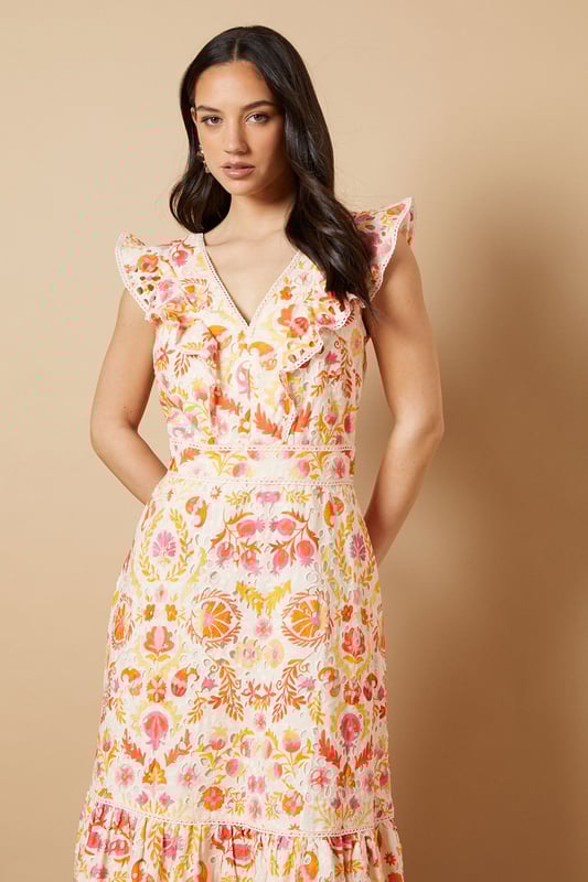 Broderie Detail V neck Midi Dress Feminine V-neckline with delicate broderie anglaise detailing
Charming flutter sleeves with ruffle trim for a playful touch
Flattering midi length with tiered hem for added movement
Defined waistband creates a beautifully structured silhouette
Striking open back design with decorative ruffle detail
This enchanting broderie detail midi dress from Oasis captures the essence of effortless daytime elegance. The intricate broderie anglaise combined with the floral pattern creates a wonderfully feminine aesthetic that's perfect for summer gatherings. Style with strappy sandals and statement earrings as seen on our model for casual brunches or garden parties. The tiered hem adds a touch of whimsy to your movement, while the defined waistband accentuates your figure beautifully. For cooler days, layer with a lightweight denim jacket and pair with white trainers for a relaxed weekend look. This versatile piece transitions seamlessly from family lunches to afternoon strolls, offering both comfort and style for your everyday wardrobe.