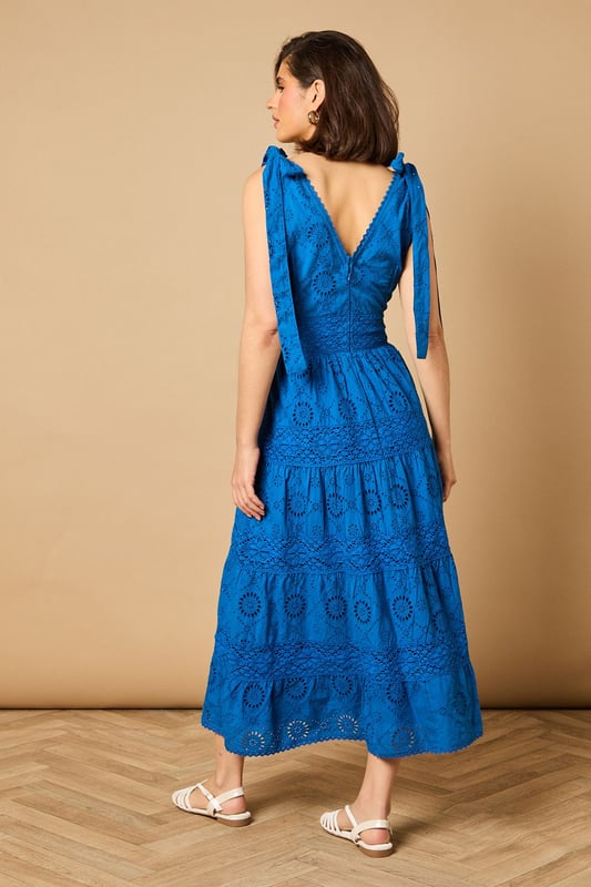 Intricate broderie anglaise detailing throughout for a feminine touch
        Flattering V-neckline at front and back for an elegant silhouette
        Charming tie shoulder straps that add a playful detail
        Tiered midi-length skirt with a relaxed, flowing shape
        Defined waistband that creates a beautifully structured fit
    
    This delightful broderie midi dress from Oasis captures effortless summer style with its feminine details and comfortable fit. The tie shoulders allow for a customised fit whilst adding a whimsical touch to the overall design. Perfect for daytime occasions, style with flat sandals as shown for a relaxed garden party or family lunch. For cooler days, layer with a lightweight denim jacket and trainers for a casual weekend look. The versatile design transitions beautifully from a countryside walk to an afternoon tea with friends. Accessorise with simple gold jewellery and a woven bag to complement the dress's intricate texture. The midi length offers both comfort and sophistication, making this a wardrobe staple that will see you through numerous casual events with ease and grace.