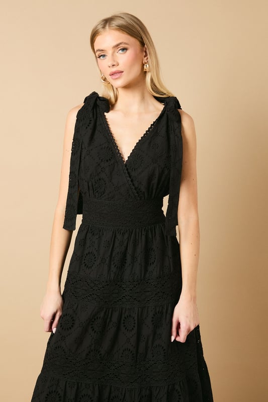 Intricate broderie anglaise detailing throughout for a feminine touch
        Flattering V-neckline at front and back for an elegant silhouette
        Charming tie shoulder straps that add a playful detail
        Tiered midi-length skirt with a relaxed, flowing shape
        Defined waistband that creates a beautifully structured fit
    
    This delightful broderie midi dress from Oasis captures effortless summer style with its feminine details and comfortable fit. The tie shoulders allow for a customised fit whilst adding a whimsical touch to the overall design. Perfect for daytime occasions, style with flat sandals as shown for a relaxed garden party or family lunch. For cooler days, layer with a lightweight denim jacket and trainers for a casual weekend look. The versatile design transitions beautifully from a countryside walk to an afternoon tea with friends. Accessorise with simple gold jewellery and a woven bag to complement the dress's intricate texture. The midi length offers both comfort and sophistication, making this a wardrobe staple that will see you through numerous casual events with ease and grace.
