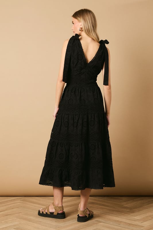 Intricate broderie anglaise detailing throughout for a feminine touch
        Flattering V-neckline at front and back for an elegant silhouette
        Charming tie shoulder straps that add a playful detail
        Tiered midi-length skirt with a relaxed, flowing shape
        Defined waistband that creates a beautifully structured fit
    
    This delightful broderie midi dress from Oasis captures effortless summer style with its feminine details and comfortable fit. The tie shoulders allow for a customised fit whilst adding a whimsical touch to the overall design. Perfect for daytime occasions, style with flat sandals as shown for a relaxed garden party or family lunch. For cooler days, layer with a lightweight denim jacket and trainers for a casual weekend look. The versatile design transitions beautifully from a countryside walk to an afternoon tea with friends. Accessorise with simple gold jewellery and a woven bag to complement the dress's intricate texture. The midi length offers both comfort and sophistication, making this a wardrobe staple that will see you through numerous casual events with ease and grace.