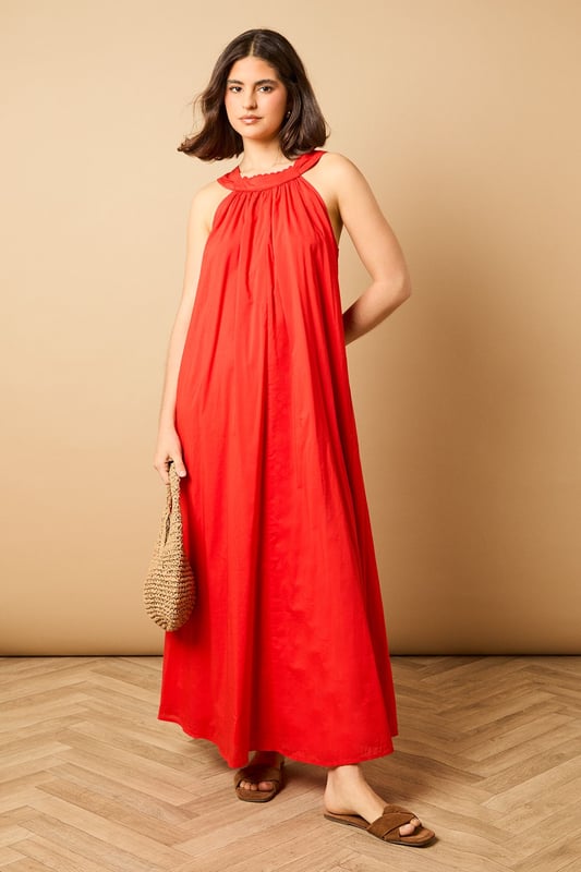 Elegant halterneck design with delicate ruffle trim detail
        Flowing maxi length for graceful movement
        Relaxed smock silhouette offering effortless comfort
        Lightweight cotton voile fabric perfect for warmer days
        Tie-back fastening for an adjustable, secure fit
    
    This breezy halterneck maxi dress captures the essence of carefree summer style with its billowing smock silhouette. The soft ruffle trim around the neckline adds a touch of feminine charm, whilst the flowing fabric creates a beautifully relaxed drape that moves gracefully with every step. Style with flat sandals as seen on our model for daytime outings, or dress up with espadrille wedges and statement earrings for garden parties and alfresco dining. The versatile design makes it ideal for family gatherings, weekend brunches or holiday packing - simply throw on with a denim jacket and crossbody bag for an effortlessly chic look that transitions seamlessly from day to evening. The lightweight fabric ensures all-day comfort, whether you're strolling along the beach or enjoying a casual lunch with friends.