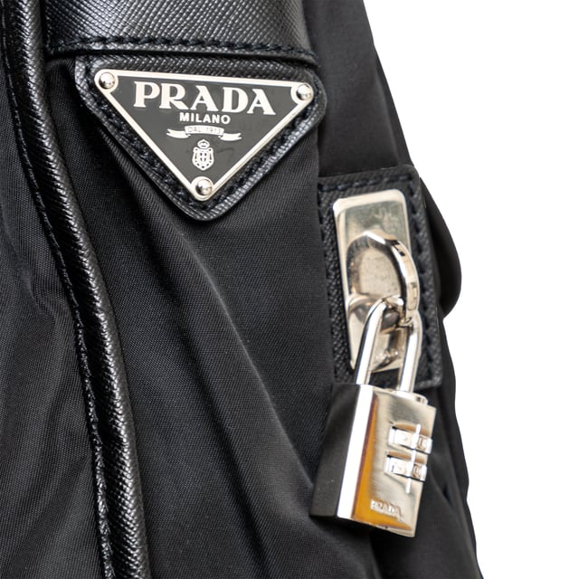 VINTAGE, RRP AS NEW
This black re-nylon messenger bag with trim features dual buckle closures on pockets, a side lock, and an enamel triangle signature brand emblem for a sleek finish.
Inclusion: dust bag
Remarks: there are some signs of wear on the hardware. Measurments:  width: 965 mm height: 812 mm