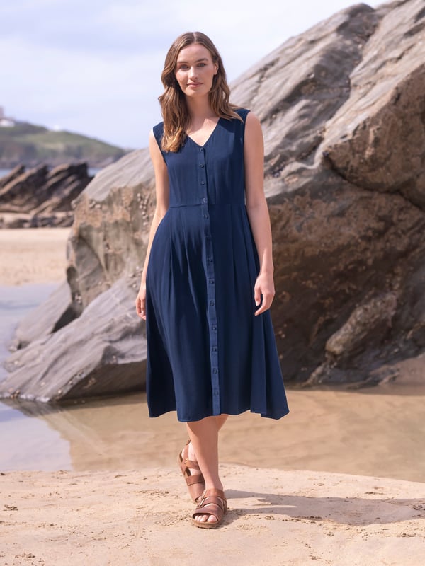 This flattering dress features a gently fitted bodice to the waist, a V neckline, and a flared skirt. The full-length button-through detail is fastened with Corozo nut buttons, while two side pockets offer practicality. Crafted from a smooth, soft and drapey woven material, this dress combines simplicity and comfort seamlessly.