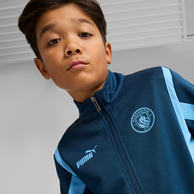 PRODUCT STORY: Young Cityzens, express your pride with this PUMA jacket featuring a multi-layered Man City silicone badge, flatlock stitching, and a PUMA Cat logo on the chest. The elasticated waistband and cuffs ensure a snug fit. Feel the Etihad Stadium energy and represent the Sky Blues with every step you take. DETAILS: Regular fit; Spacer material; Flatlock stitching; Hood; Full zip; Long sleeves; Elasticated waistband and cuffs; Multi-layered Manchester City silicone badge; PUMA Cat logo on the chest; PUMA Youth: Recommended for older kids between 8 and 16 years.