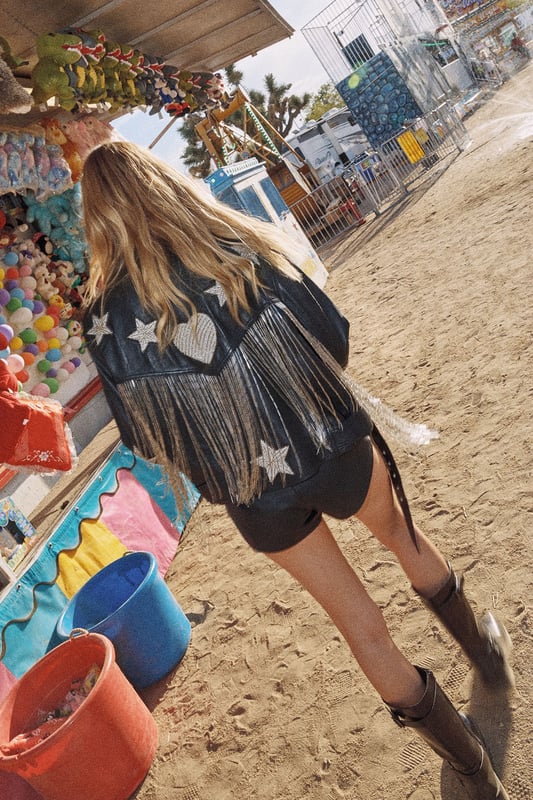 Genuine leather jacket featuring playful star and heart-shaped patches for distinctive character
        Statement metallic tassels cascade down the back for dramatic movement and flair
        Boxy, oversized silhouette offers a relaxed fit perfect for layering
        Classic biker-style design with notched lapels and asymmetric zip closure
        Fully lined interior ensures comfort and durability for long-lasting wear
    
    Make a bold statement with this eye-catching leather jacket from Nasty Gal. The oversized, boxy fit creates a contemporary silhouette that pairs brilliantly with both casual and evening looks. The striking tassel detail adds movement and drama to your ensemble, whilst the whimsical star and heart patches infuse a touch of playfulness into this edgy piece. Style with shorts and a crop top as shown for festival-ready vibes, or throw over a slip dress with chunky boots for an unforgettable night out look. Perfect for those who aren't afraid to stand out, this jacket works brilliantly for club nights, drinks with friends, or any urban adventure where you want to showcase your distinctive style. The versatile design allows for year-round wear - layer over knitwear during cooler months or drape over your shoulders on chilly summer evenings.