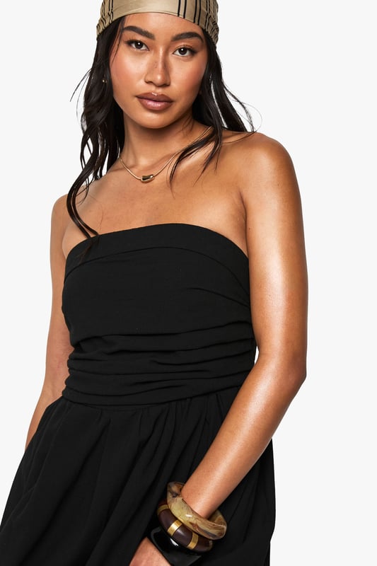 Chic bandeau neckline with a single shoulder strap for added support
        Flattering gathered waistband that defines your silhouette
        Flowing midi-length skirt with elegant side slit for ease of movement
        Lightweight linen-look fabric perfect for warm-weather occasions
        Versatile design that can be dressed up or down for various events
    
    This bandeau midi dress combines effortless style with practical comfort for your casual wardrobe. The striking asymmetric strap detail adds a contemporary twist to the classic bandeau design, while the gathered waistband creates a flattering shape that complements all figures. Style with flat sandals and a beanie for a relaxed daytime look, as shown by our model, or swap for kitten heels and statement jewellery for family gatherings. The side slit offers both practical movement and a subtle flash of leg, making this dress ideal for garden parties or brunches with friends. Layer with a denim jacket when the temperature drops or add a crossbody bag to keep your essentials close while maintaining the dress's clean lines. This Boohoo staple will quickly become your go-to for those "nothing to wear" moments.