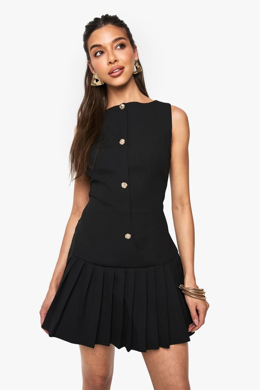 Sleeveless mini dress with elegant slash neckline for a sophisticated silhouette
        Decorative button detail running down the front adds a chic, structured element
        Pleated skirt creates playful movement and a flattering flare
        Fitted waist design accentuates your natural shape
        Versatile crepe fabric offers comfortable stretch whilst maintaining structure
    
    This striking mini dress from Boohoo combines classic tailoring with contemporary flair. The fitted bodice with its distinctive button detailing creates a polished look, while the pleated skirt adds a touch of playfulness perfect for evening adventures. Style with strappy heels and statement earrings as shown for a night at the club, or dress down with chunky trainers and an oversized denim jacket for casual drinks with friends. The versatile design transitions effortlessly from day to night - pair with a tailored blazer for impromptu after-work gatherings or showcase on its own with a mini handbag for those spontaneous nights out. The structured yet comfortable fit makes this dress a reliable go-to when you want to make an impression whilst feeling confident on the dance floor.