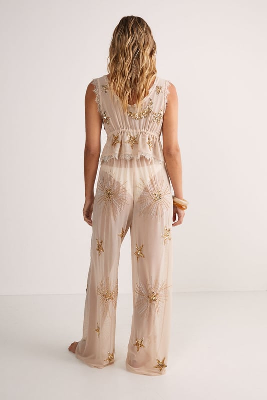 Enchanting moon and star embellishments
        Sheer mesh fabric for a sultry look
        Tie-front design for adjustable fit
        Delicate lace trim detailing
        Versatile waistcoat style for layering
    
    Embrace celestial chic with this captivating Embellished Moon & Star Tie Front Beach Waistcoat from NastyGal. Perfect for those balmy beach days or lounging by the pool, this sheer mesh waistcoat radiates bohemian glamour. The alluring V-neckline and tie-front closure allow for a customisable fit, while the intricate lace trim adds a touch of romance. Style it over your favourite swimsuit for an effortlessly chic beach look, or layer it over a slip dress for a dreamy night-time ensemble. The versatile nature of this piece makes it an essential addition to your holiday wardrobe, seamlessly transitioning from daytime beachwear to evening drinks by the sea. Let the shimmering moon and star embellishments catch the light as you dance under the stars, embodying the free-spirited essence of summer nights.