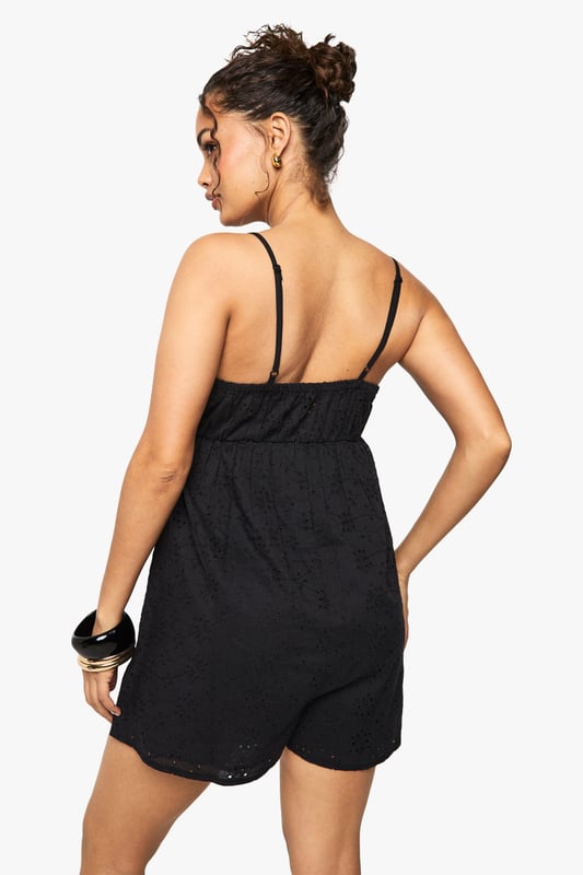 Crafted from delicate broderie anglaise fabric with intricate eyelet detailing
        Feminine V-neckline with scalloped trim for a romantic touch
        Adjustable spaghetti straps for a customised fit
        Relaxed silhouette with a flattering empire waistline
        Lightweight design perfect for warm-weather occasions
    
    This charming broderie anglaise playsuit from Boohoo combines comfort with effortless style. The delicate eyelet pattern and scalloped trim create a feminine aesthetic that works beautifully for daytime events. Style with flat sandals and stacked bangles as shown for casual gatherings, or dress up with espadrille wedges and a woven clutch for garden parties. The relaxed fit makes it ideal for family barbecues or weekend brunches, while the all-in-one design offers practicality without compromising on style. For cooler evenings, layer with a lightweight denim jacket and switch to ankle boots for versatility that transitions through the seasons. This playsuit embodies carefree summer dressing with its easy-to-wear appeal and timeless broderie fabric.