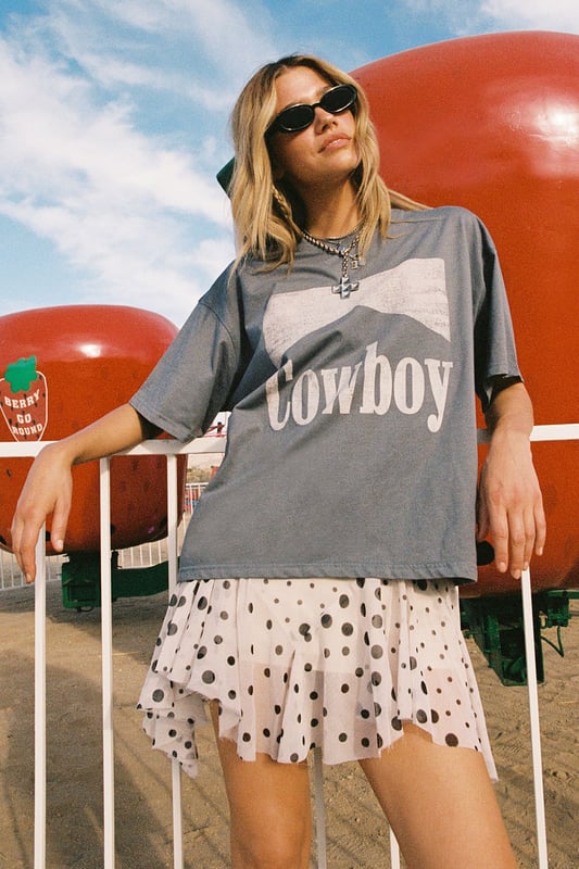 Oversized fit with relaxed dropped shoulders for effortless comfort
        Bold 'Cowboy' graphic print across the front for statement appeal
        Versatile crew neckline that works with multiple accessories
        Short sleeves with a casual, unfinished look for laid-back styling
        Cotton fabric offering breathability and softness for all-day wear
    
    Channel your inner western spirit with this Nasty Gal Cowboy Oversized Graphic T-Shirt. The relaxed silhouette creates the perfect canvas for casual daywear, whilst the statement graphic adds character to your ensemble. Style it as shown with a flirty polka dot skirt and ankle boots for a playful contrast between rugged and feminine aesthetics. For cooler days, layer with an oversized denim jacket and add chunky jewellery to enhance the look. This versatile piece transitions seamlessly from festival grounds to weekend brunches or casual shopping trips with friends. The cotton construction ensures comfort throughout the day, making it an essential addition to your casual wardrobe rotation. Pair with your favourite trainers for an effortlessly cool daytime look.