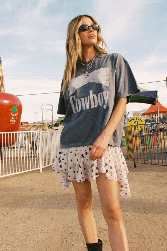 Oversized fit with relaxed dropped shoulders for effortless comfort
        Bold 'Cowboy' graphic print across the front for statement appeal
        Versatile crew neckline that works with multiple accessories
        Short sleeves with a casual, unfinished look for laid-back styling
        Cotton fabric offering breathability and softness for all-day wear
    
    Channel your inner western spirit with this Nasty Gal Cowboy Oversized Graphic T-Shirt. The relaxed silhouette creates the perfect canvas for casual daywear, whilst the statement graphic adds character to your ensemble. Style it as shown with a flirty polka dot skirt and ankle boots for a playful contrast between rugged and feminine aesthetics. For cooler days, layer with an oversized denim jacket and add chunky jewellery to enhance the look. This versatile piece transitions seamlessly from festival grounds to weekend brunches or casual shopping trips with friends. The cotton construction ensures comfort throughout the day, making it an essential addition to your casual wardrobe rotation. Pair with your favourite trainers for an effortlessly cool daytime look.