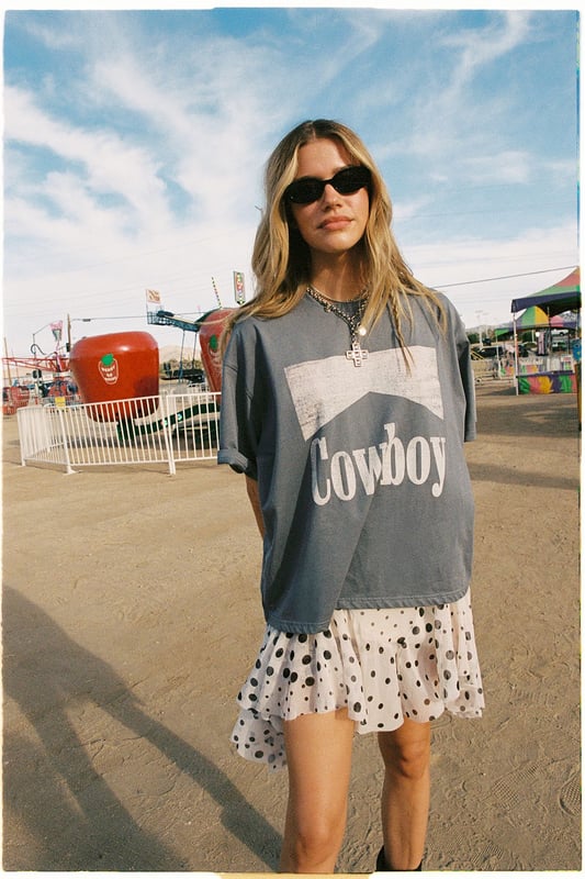 Oversized fit with relaxed dropped shoulders for effortless comfort
        Bold 'Cowboy' graphic print across the front for statement appeal
        Versatile crew neckline that works with multiple accessories
        Short sleeves with a casual, unfinished look for laid-back styling
        Cotton fabric offering breathability and softness for all-day wear
    
    Channel your inner western spirit with this Nasty Gal Cowboy Oversized Graphic T-Shirt. The relaxed silhouette creates the perfect canvas for casual daywear, whilst the statement graphic adds character to your ensemble. Style it as shown with a flirty polka dot skirt and ankle boots for a playful contrast between rugged and feminine aesthetics. For cooler days, layer with an oversized denim jacket and add chunky jewellery to enhance the look. This versatile piece transitions seamlessly from festival grounds to weekend brunches or casual shopping trips with friends. The cotton construction ensures comfort throughout the day, making it an essential addition to your casual wardrobe rotation. Pair with your favourite trainers for an effortlessly cool daytime look.