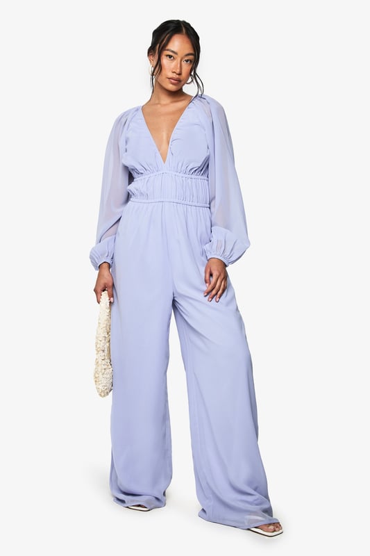 Elegant chiffon jumpsuit featuring a plunging V-neckline for a striking silhouette
        Ruched waistband detail creates a flattering, defined waist
        Dramatic wide-leg design offers comfortable movement and a fashion-forward look
        Billowing long sleeves with gathered cuffs add romantic flair
        Flowing fabric drapes beautifully for an effortlessly chic appearance
    
    Make a statement at your next night out in this show-stopping wide-leg jumpsuit. The plunging V-neckline creates an alluring focal point, whilst the ruched waistband cinches you in at just the right spot for a figure-enhancing effect. The billowing sleeves and flowing wide legs create a beautifully balanced silhouette that moves gracefully as you do. Style with strappy heels and a woven clutch, as shown, for drinks with the girls, or dress it up with statement earrings and metallic accessories for special occasions. This versatile Boohoo piece transitions seamlessly from cocktail bars to dance floors, ensuring you'll stand out for all the right reasons. Perfect for those who want to combine comfort with head-turning style for their evening adventures.