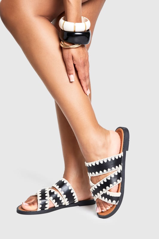 Contrast Blanket Stitch Crossover Sandals Striking contrast cross-over design with distinctive zig-zag stitching detail
Comfortable flat heel measuring between 0-2cm for all-day wear
Open-toe silhouette with dual cross-over straps for a secure fit
Durable PU construction with textured sole for added grip
Slip-on style for effortless wearing and removal
These eye-catching cross-over sandals bring a touch of artisanal flair to your casual wardrobe. The distinctive contrast stitching creates a bold visual statement whilst maintaining a relaxed vibe perfect for summer styling. Pair with cropped linen trousers and an oversized shirt for daytime outings, or team with a flowing maxi dress for garden parties and family gatherings. The flat design ensures comfort for extended wear, making these sandals ideal for city explorations or beachside strolls. Their versatile aesthetic works brilliantly with both neutral and vibrant ensembles, allowing you to customise your look according to the occasion. A statement bangle, as shown on the model, completes the look with a contemporary twist - the perfect finishing touch for these Boohoo sandals that balance style and practicality with effortless charm.