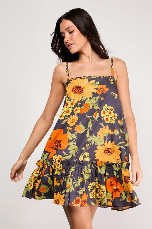 Distinctive plaited straps add a unique textural element to this breezy sundress
        Relaxed A-line silhouette with a feminine flounced hem for added movement
        Square neckline creates a flattering frame for the dcolletage
        Lightweight cotton poplin fabric ensures comfort during warmer days
        Bold floral print makes a confident statement while maintaining versatility
    
    This effortlessly chic sundress captures the essence of carefree summer style with its relaxed silhouette and eye-catching floral pattern. The plaited straps offer a distinctive design element that sets this piece apart, while the flounced hem adds a playful touch to your movement. Style with flat sandals as shown for daytime outings or family gatherings, or dress up with espadrille wedges and statement earrings for garden parties. The cotton poplin fabric ensures breathability during warmer weather, making this an ideal choice for holidays abroad or weekend brunches. Layer with a cropped denim jacket when temperatures cool, or wear over a fitted tee for a contemporary layered look. This versatile sundress transitions seamlessly from casual daytime events to relaxed evening occasions with just a few accessory changes.