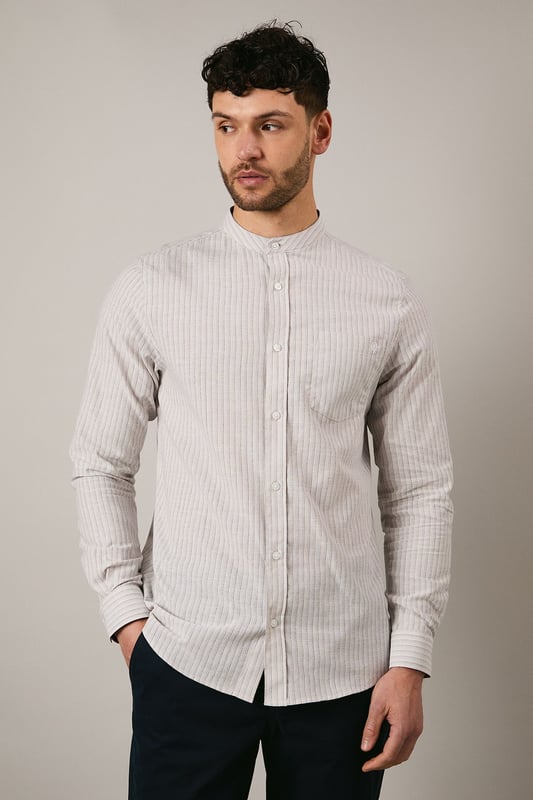 Off White Stripe Grandad Collar Long Sleeve Shirt Distinctive grandad collar design for a contemporary twist on classic shirting
Subtle stripe pattern woven throughout the fabric for understated visual interest
Long sleeves with buttoned cuffs offering versatile styling options
Chest pocket detail adding functional practicality to the design
Relaxed fit with a curved hem perfect for both tucked and untucked styling
This Maine grandad collar shirt combines timeless appeal with modern sensibility. The clean-lined design makes it an effortless addition to your casual wardrobe, whilst the distinctive collar creates a relaxed yet refined aesthetic. Style with dark trousers and loafers as shown for family gatherings or weekend brunches. For a more laid-back approach, pair with chinos and trainers for everyday wear. The versatile nature of this shirt makes it ideal for transitional weather - layer under a lightweight jacket when temperatures drop or wear alone with rolled sleeves during warmer days. The button-through front and woven fabric ensure comfort and ease of movement, making this shirt a practical choice for various casual occasions without compromising on style.