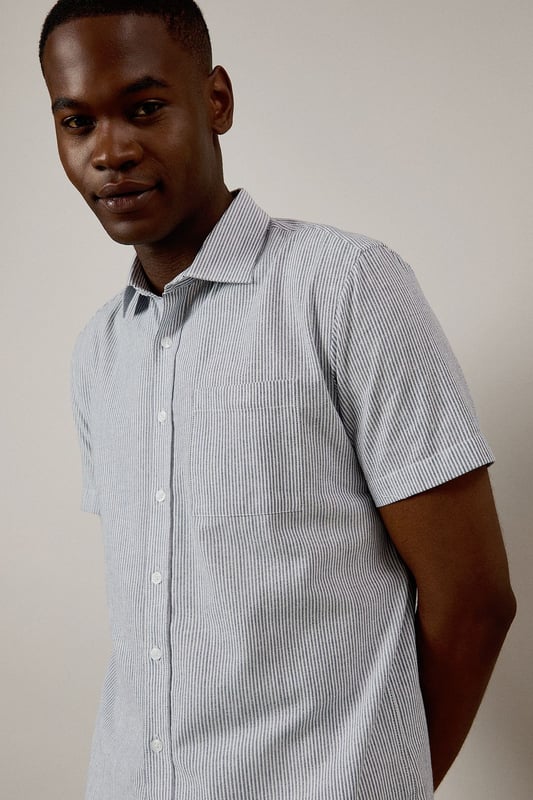 Navy Fine Stripe Short Sleeve Shirt Classic fine stripe pattern for a refined casual look
Short sleeves with neat hems for warm-weather comfort
Traditional collar with structured shape
Convenient chest pocket for added functionality
Regular fit design offering ease of movement throughout the day
This Burton short sleeve shirt combines timeless style with everyday practicality. The fine stripe pattern creates visual interest while maintaining versatility for various occasions. Pair with chino shorts and loafers as shown for a smart casual weekend look perfect for beer garden gatherings or family barbecues. For cooler evenings, layer under a lightweight jumper or team with dark denim jeans and trainers for pub outings with mates. The woven fabric offers breathability and comfort during sporting events or casual match viewings. This shirt transitions effortlessly from daytime casual to evening socialising, making it an essential addition to any practical British wardrobe. A reliable choice for the man who values classic style with contemporary appeal.