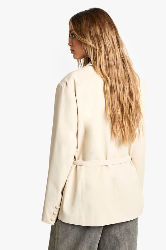 Oversized blazer featuring elegant peak lapels for a sophisticated silhouette
        Distinctive gathered waist detail with tie fastening to create a flattering shape
        Functional front pockets add practicality to this statement piece
        Long sleeves with subtle button detailing at the cuffs
        Versatile woven fabric that maintains structure while offering comfort
    
    Make a bold statement with this contemporary oversized blazer from Boohoo. The gathered waist detail creates a feminine silhouette while maintaining the powerful presence of tailored outerwear. Perfect for formal occasions, pair with tailored trousers and heels for graduations or wedding receptions. For race day elegance, style with a fascinator and a sleek clutch bag. The versatility of this piece also lends itself to more casual styling - as seen on our model with relaxed grey trousers and a headscarf for an effortlessly chic daytime look. The oversized fit offers room for layering over fine knitwear during cooler months, while the tie waist allows you to customise the silhouette to your preference. This blazer bridges the gap between structured formality and contemporary fashion, making it an essential addition to your occasion wardrobe.