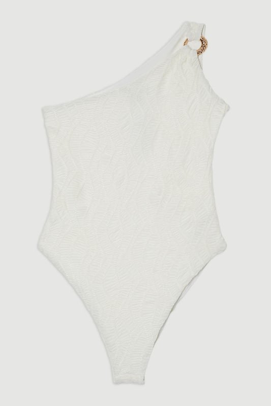 Make a statement poolside in this Karen Millen textured swimsuit that combines sophistication with modern design elements. The asymmetric one-shoulder neckline creates a dramatic focal point, enhanced by the luxe metallic hardware detail. The distinctive cut-out adds intrigue while maintaining a flattering shape. The textured fabric offers visual interest and dimension that catches the light beautifully as you move. Style with oversized sunglasses and gold-toned jewellery for lounging by the pool, or pair with a flowing maxi skirt and sandals for beachside dining. This versatile piece transitions effortlessly from daytime swimming to sunset cocktails when worn as a bodysuit with wide-leg trousers. Perfect for your summer holiday wardrobe, this swimsuit delivers both style and substance for confident beach days.   Striking one-shoulder design with metallic hardware detail Textured fabric creates a sophisticated dimensional effect Strategic cut-out detail adds a contemporary twist Fully lined for comfort and confidence Sculpting fit that flatters the silhouette