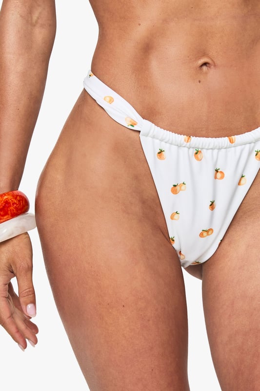 Tangerine Print Ruched Bikini Brief Ruched thong bikini bottoms with playful tangerine print for a fresh summer aesthetic
Adjustable side ties for a customisable fit that flatters your figure
High-cut leg design to elongate your silhouette
Minimal coverage back for a contemporary beach look
Pairs perfectly with the matching underwired bikini top for a coordinated swimwear set
Make a splash this season in these eye-catching ruched thong bikini bottoms from Boohoo. The delightful tangerine print adds a zesty touch to your beach attire, whilst the ruched detailing creates texture and visual interest. The high-cut leg design works to lengthen your silhouette, whilst the thong back offers a daring, contemporary look perfect for maximising your tan. Style with the matching underwired top and add statement accessories like bold bangles for a complete beach-ready ensemble. These versatile bottoms transition effortlessly from poolside lounging to beachfront strolls. For a fashion-forward look, throw on a sheer cover-up and strappy sandals when heading to a beach bar. Ideal for summer holidays, festivals, or simply soaking up the sun closer to home.