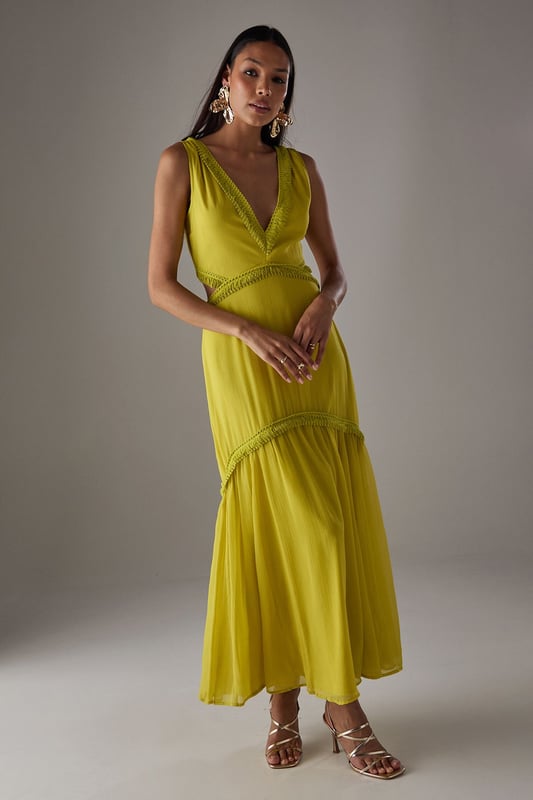 Flowing chiffon maxi dress with delicate fringe trim detailing
        Striking plunge neckline creates a feminine silhouette
        Elegant cut-out back design with tie fastening for adjustable fit
        Tiered skirt construction with gathered waist for added movement
        Fully lined for comfort and opacity while maintaining the lightweight feel
    
    Make a statement in this captivating chiffon maxi dress from Warehouse. The striking plunge neckline frames the dcolletage beautifully, while the cut-out back detail adds an unexpected twist to this flowing piece. The delicate fringe trim and tiered construction create movement with every step, making it perfect for garden parties or summer soires. Style with metallic strappy heels and statement earrings as seen on our model for evening events, or dress down with flat sandals and a woven clutch for daytime gatherings. The lightweight fabric drapes elegantly around the figure, creating a relaxed yet refined silhouette that works wonderfully for warm-weather occasions. This versatile dress transitions effortlessly from casual family gatherings to more formal events with the right accessories.