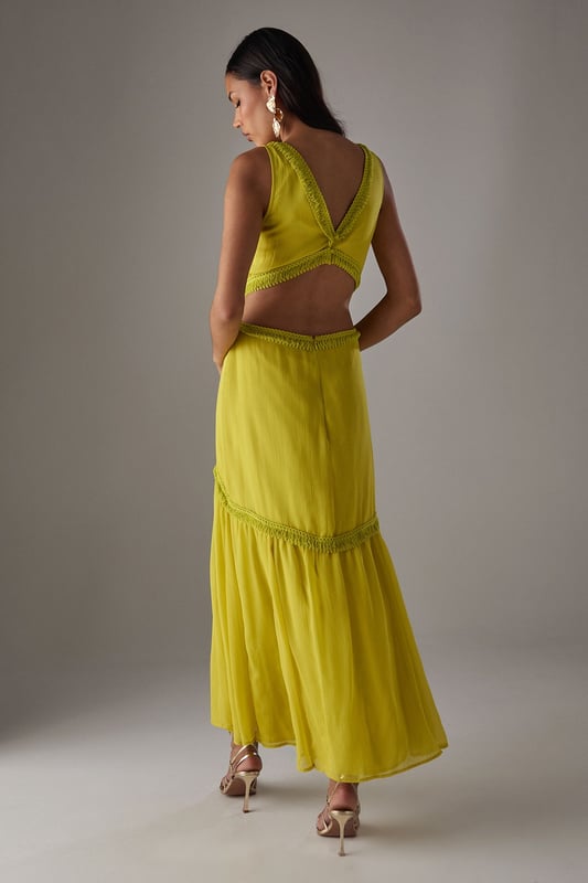 Flowing chiffon maxi dress with delicate fringe trim detailing
        Striking plunge neckline creates a feminine silhouette
        Elegant cut-out back design with tie fastening for adjustable fit
        Tiered skirt construction with gathered waist for added movement
        Fully lined for comfort and opacity while maintaining the lightweight feel
    
    Make a statement in this captivating chiffon maxi dress from Warehouse. The striking plunge neckline frames the dcolletage beautifully, while the cut-out back detail adds an unexpected twist to this flowing piece. The delicate fringe trim and tiered construction create movement with every step, making it perfect for garden parties or summer soires. Style with metallic strappy heels and statement earrings as seen on our model for evening events, or dress down with flat sandals and a woven clutch for daytime gatherings. The lightweight fabric drapes elegantly around the figure, creating a relaxed yet refined silhouette that works wonderfully for warm-weather occasions. This versatile dress transitions effortlessly from casual family gatherings to more formal events with the right accessories.