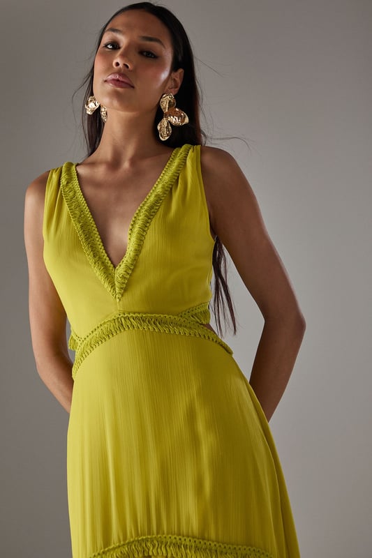 Flowing chiffon maxi dress with delicate fringe trim detailing
        Striking plunge neckline creates a feminine silhouette
        Elegant cut-out back design with tie fastening for adjustable fit
        Tiered skirt construction with gathered waist for added movement
        Fully lined for comfort and opacity while maintaining the lightweight feel
    
    Make a statement in this captivating chiffon maxi dress from Warehouse. The striking plunge neckline frames the dcolletage beautifully, while the cut-out back detail adds an unexpected twist to this flowing piece. The delicate fringe trim and tiered construction create movement with every step, making it perfect for garden parties or summer soires. Style with metallic strappy heels and statement earrings as seen on our model for evening events, or dress down with flat sandals and a woven clutch for daytime gatherings. The lightweight fabric drapes elegantly around the figure, creating a relaxed yet refined silhouette that works wonderfully for warm-weather occasions. This versatile dress transitions effortlessly from casual family gatherings to more formal events with the right accessories.