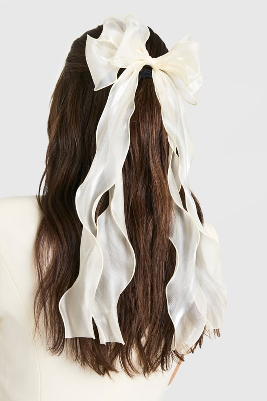 Oversized bow design for a statement look
        Sheer organza fabric creates an ethereal effect
        Long, flowing ribbons for added movement
        Secure metal clip for easy attachment
        Versatile accessory suitable for various hairstyles
    
    Add a touch of whimsy to your ensemble with this enchanting organza hair bow. The oversized design commands attention, while the sheer fabric lends an air of delicate sophistication. Perfect for casual outings or family gatherings, this accessory effortlessly elevates any look. Style it with loose waves for a romantic vibe, or use it to accent a sleek ponytail for a more polished appearance. The long, flowing ribbons create a captivating effect as you move, making it ideal for those who love to make a subtle yet striking impression. Whether you're headed to a picnic in the park or a laid-back brunch with friends, this versatile hair bow is sure to become a go-to piece in your accessory collection.