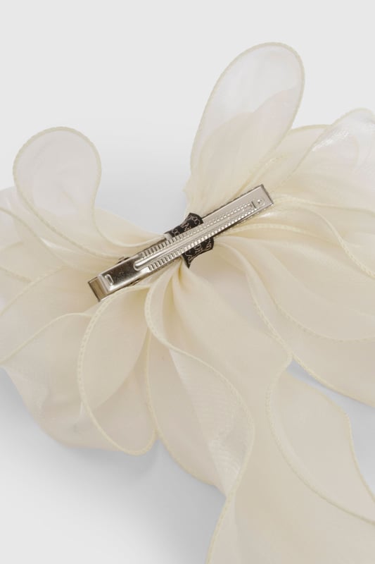 Oversized bow design for a statement look
        Sheer organza fabric creates an ethereal effect
        Long, flowing ribbons for added movement
        Secure metal clip for easy attachment
        Versatile accessory suitable for various hairstyles
    
    Add a touch of whimsy to your ensemble with this enchanting organza hair bow. The oversized design commands attention, while the sheer fabric lends an air of delicate sophistication. Perfect for casual outings or family gatherings, this accessory effortlessly elevates any look. Style it with loose waves for a romantic vibe, or use it to accent a sleek ponytail for a more polished appearance. The long, flowing ribbons create a captivating effect as you move, making it ideal for those who love to make a subtle yet striking impression. Whether you're headed to a picnic in the park or a laid-back brunch with friends, this versatile hair bow is sure to become a go-to piece in your accessory collection.