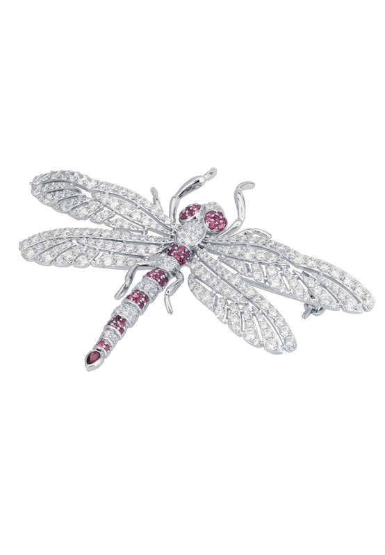 Dragonfly Brooch Silver Ruby Cz The Dragonfly Brooch is a masterfully crafted piece made from high-quality 925 sterling silver. This exquisite brooch captures the delicate beauty of a dragonfly, adorned with a dazzling array of ruby pink and white zirconia. The body of the dragonfly features alternating stripes of pink and white, along with pink eyes, creating a stunning visual contrast that is sure to catch the eye.The wings are intricately designed with a lace-like pattern, encrusted with sparkling white zirconia that shimmer with every movement. The tail of the dragonfly is elegantly finished with a larger ruby-coloured zirconia, making this brooch a true statement piece. Measuring 7.0cm in width, 5.0cm in length, and weighing a comfortable 12.7 grams, this brooch is perfect for adding a touch of glamour to any outfit.Dragonflies hold a special place in jewellery, symbolizing transformation, adaptability, and a deep connection to nature. They remind us to embrace change and live life to the fullest, making this brooch not just a beautiful accessory but a meaningful piece of art.Perfect for nature enthusiasts, lovers of fine craftsmanship, and anyone who appreciates unique and symbolic jewellery. Add the Dragonfly Brooch Silver Ruby Cz to your collection today and let its beauty and symbolism inspire you.