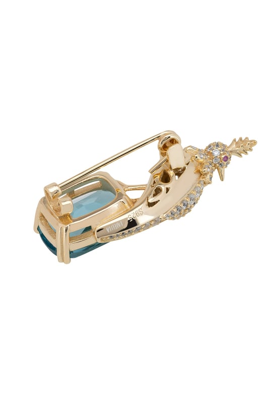 Crested Love Bird Brooch London Blue Topaz Gold Your brooch is a statement of elegance, inspired by the quiet majesty of nature. Designed in the image of a regal crested bird, this handcrafted piece is forged in 925 sterling silver and richly plated with 18ct gold for a luxurious finish that gleams with timeless beauty.Nestled beneath the zirconia-encrusted bird, a lab-created London blue topaz—cut to a refined rectangular silhouette—adds a deep, oceanic sparkle that captivates in every light. At 3.8 cm long, 1.4cm wide and just 7.0 grams in weight, your brooch wears with comfortable grace on any lapel, scarf, or dress.Whether you're accenting a formal look or adding a touch of opulence to your everyday style, your brooch offers a wearable blend of art, craftsmanship, and storytelling. This is more than an accessory—it’s a piece that speaks.