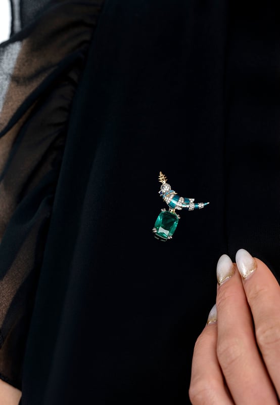 Make a graceful impression with a brooch that captures the essence of nature and the craftsmanship of fine jewellery. Inspired by the striking beauty of a crested love bird and designed for those who appreciate intricate detail and timeless elegance, it blends organic charm with elevated materials for a result that is both eye-catching and tasteful.Handcrafted from 925 sterling silver, the bird’s body is brought to life through a vivid green enamel finish, enhanced by a trail of sparkling clear zircons that catch the light with every turn. Its crest and legs are accented in lustrous gold plating, adding warmth and contrast to the design. A delicate collar of turquoise zircons encircles the neck, drawing the eye with a subtle pop of colour. Perched confidently atop a rectangular-cut lab-grown emerald, the love bird forms a stunning focal point.With dimensions of 3.0 cm in width, 3.6 cm in depth, and a weight of 7.5 grams, this brooch is perfectly sized to make a statement without overwhelming. It’s a celebration of beauty, craftsmanship, and charm in one wearable work of art.