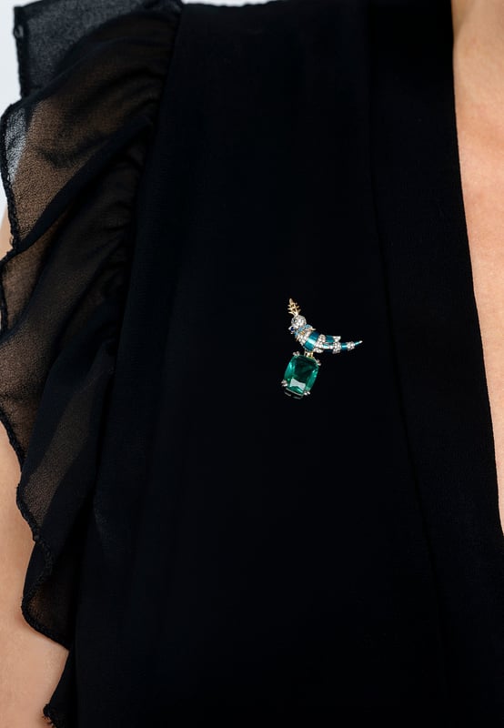 Make a graceful impression with a brooch that captures the essence of nature and the craftsmanship of fine jewellery. Inspired by the striking beauty of a crested love bird and designed for those who appreciate intricate detail and timeless elegance, it blends organic charm with elevated materials for a result that is both eye-catching and tasteful.Handcrafted from 925 sterling silver, the bird’s body is brought to life through a vivid green enamel finish, enhanced by a trail of sparkling clear zircons that catch the light with every turn. Its crest and legs are accented in lustrous gold plating, adding warmth and contrast to the design. A delicate collar of turquoise zircons encircles the neck, drawing the eye with a subtle pop of colour. Perched confidently atop a rectangular-cut lab-grown emerald, the love bird forms a stunning focal point.With dimensions of 3.0 cm in width, 3.6 cm in depth, and a weight of 7.5 grams, this brooch is perfectly sized to make a statement without overwhelming. It’s a celebration of beauty, craftsmanship, and charm in one wearable work of art.