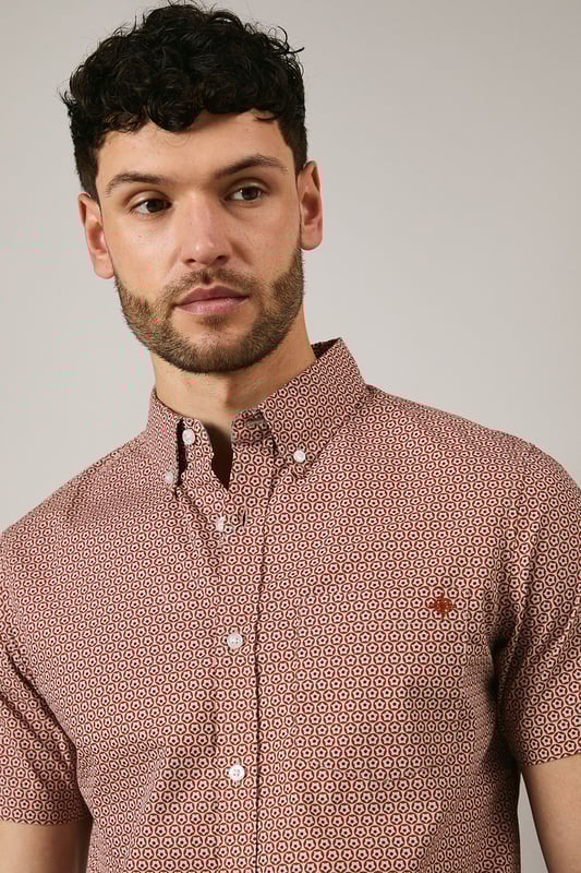Orange Geo Print Short Sleeve Shirt Distinctive geo print pattern creates visual interest across the entire shirt
Classic button-down collar for a smart-casual finish
Short sleeves with neat hems perfect for warmer weather
Signature Maine embroidered logo detail on chest
Centre back pleat for enhanced comfort and movement
This Maine geo print shirt combines contemporary pattern with timeless design for versatile summer styling. The pure cotton fabric ensures breathability and comfort throughout the day, whilst the structured button-down collar maintains a refined appearance even when worn casually. Style as seen with neutral shorts and white trainers for relaxed weekend brunches or garden gatherings. For evening socials, pair with chinos and loafers for an effortlessly sophisticated look. The subtle geometric pattern works brilliantly with solid-coloured bottoms, allowing the shirt to be the focal point of your ensemble. Perfect for holidays, casual Fridays at the office, or simply elevating your everyday wardrobe with a touch of considered pattern.